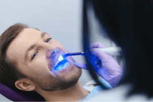 Patient receiving professional teeth whitening treatment with blue LED light.